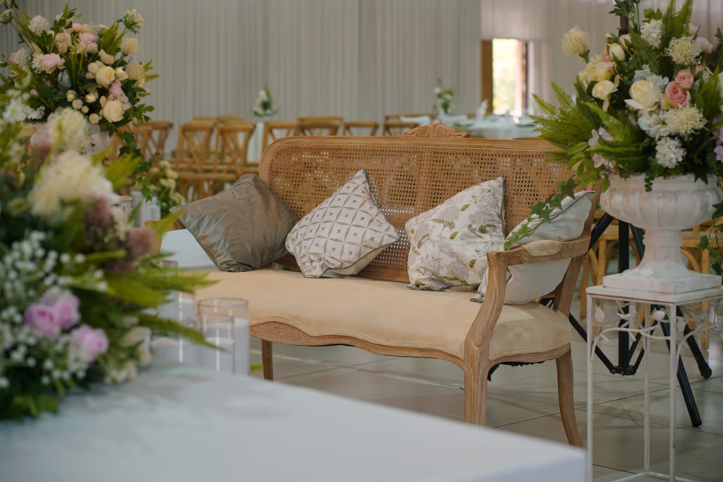 A cane settee framed by soft floral arrangements
